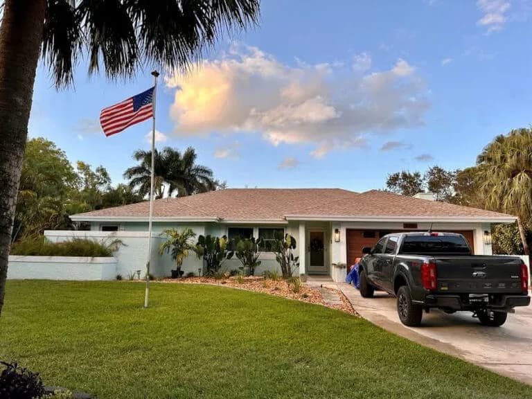 Florida home with a tan architectural shingle roof and an American flag at dusk